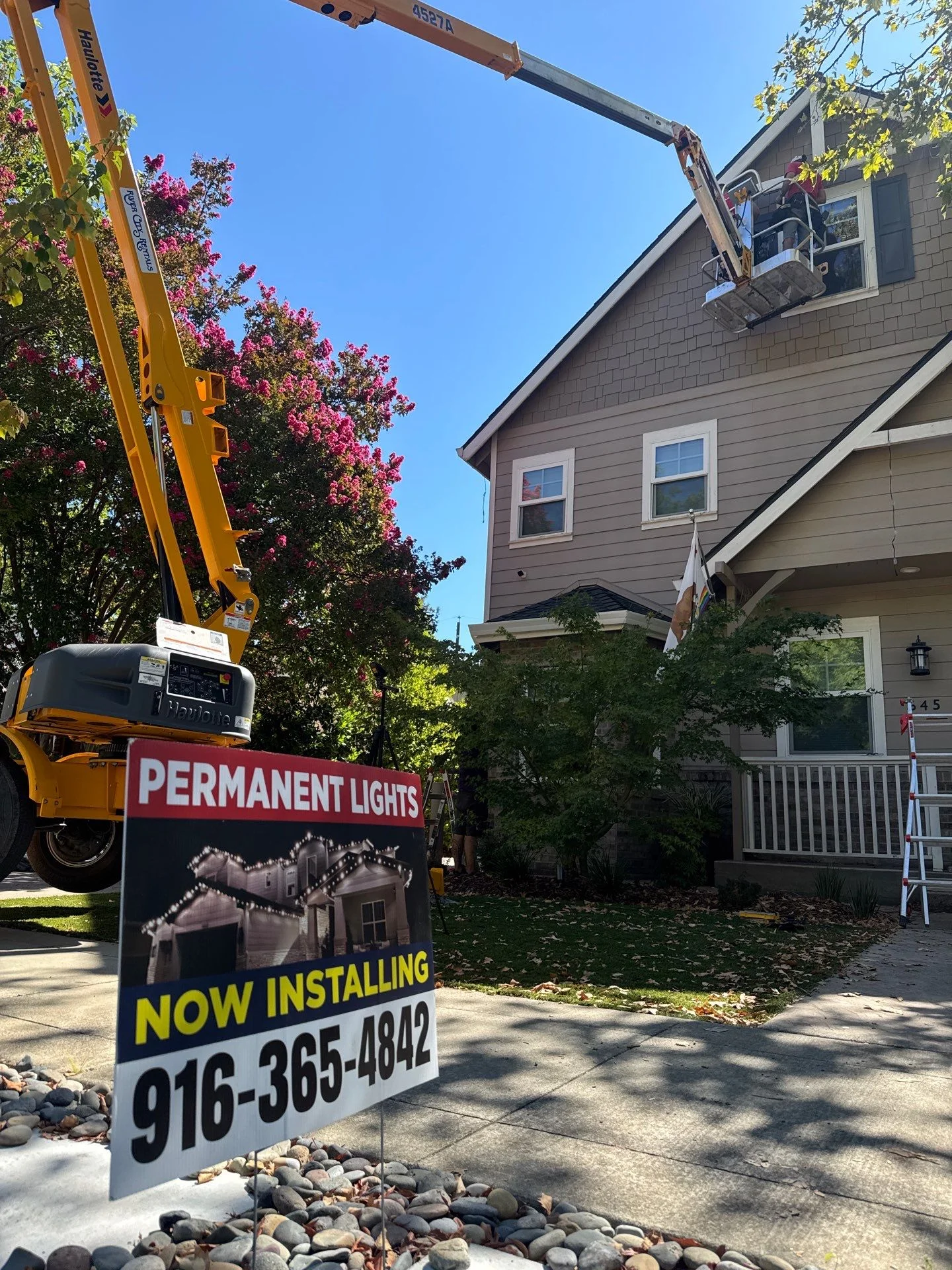 Santa's Lights crew working from a boom lift basket at the peak of an East Sacramento craftsman home