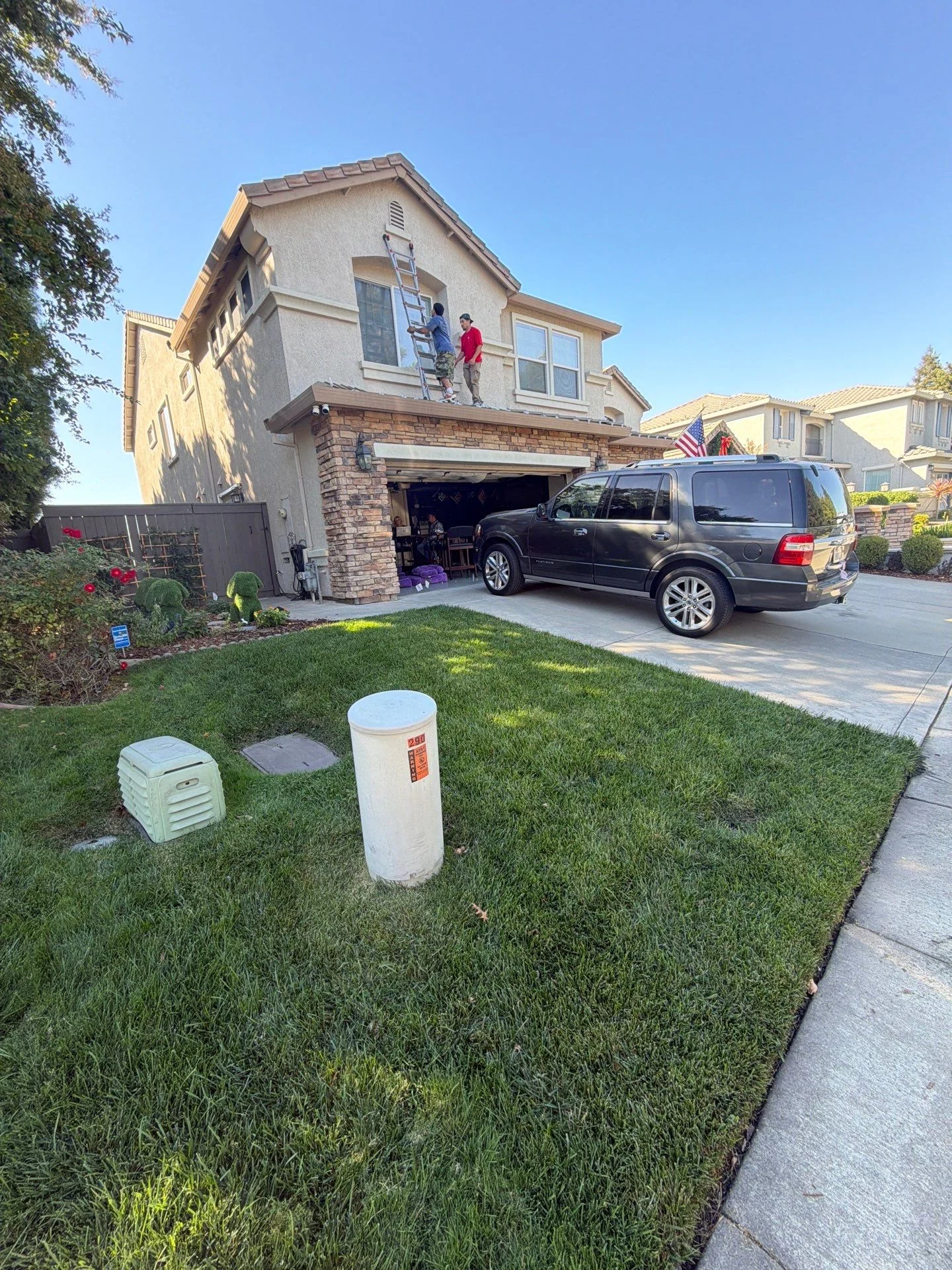 Two Santa's Lights crew members on a ladder installing lights on a tile roof home in North Natomas