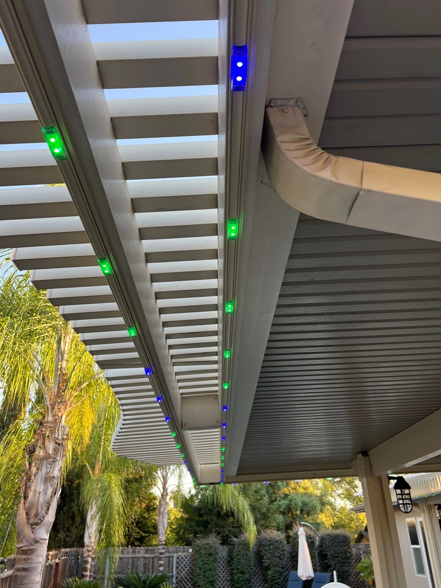 Permanent lighting track along the beams of an aluminum lattice patio cover with green and blue lights lit