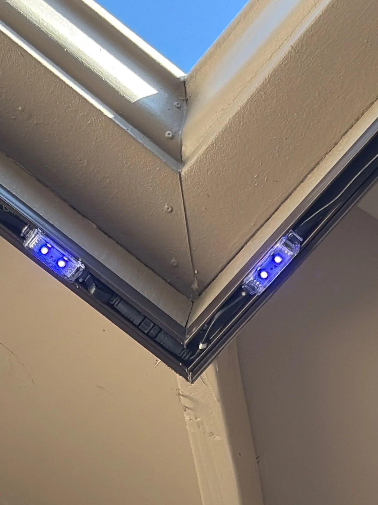 Close-up of a permanent lighting fixture glowing blue at a mitered roof corner on a stucco home