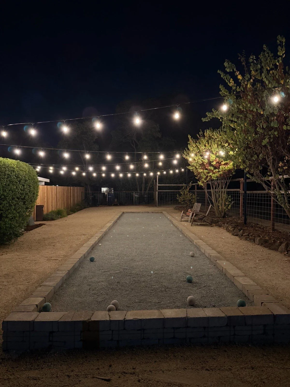 Backyard bocce court with layered bistro string lights glowing at night in Fair Oaks, California