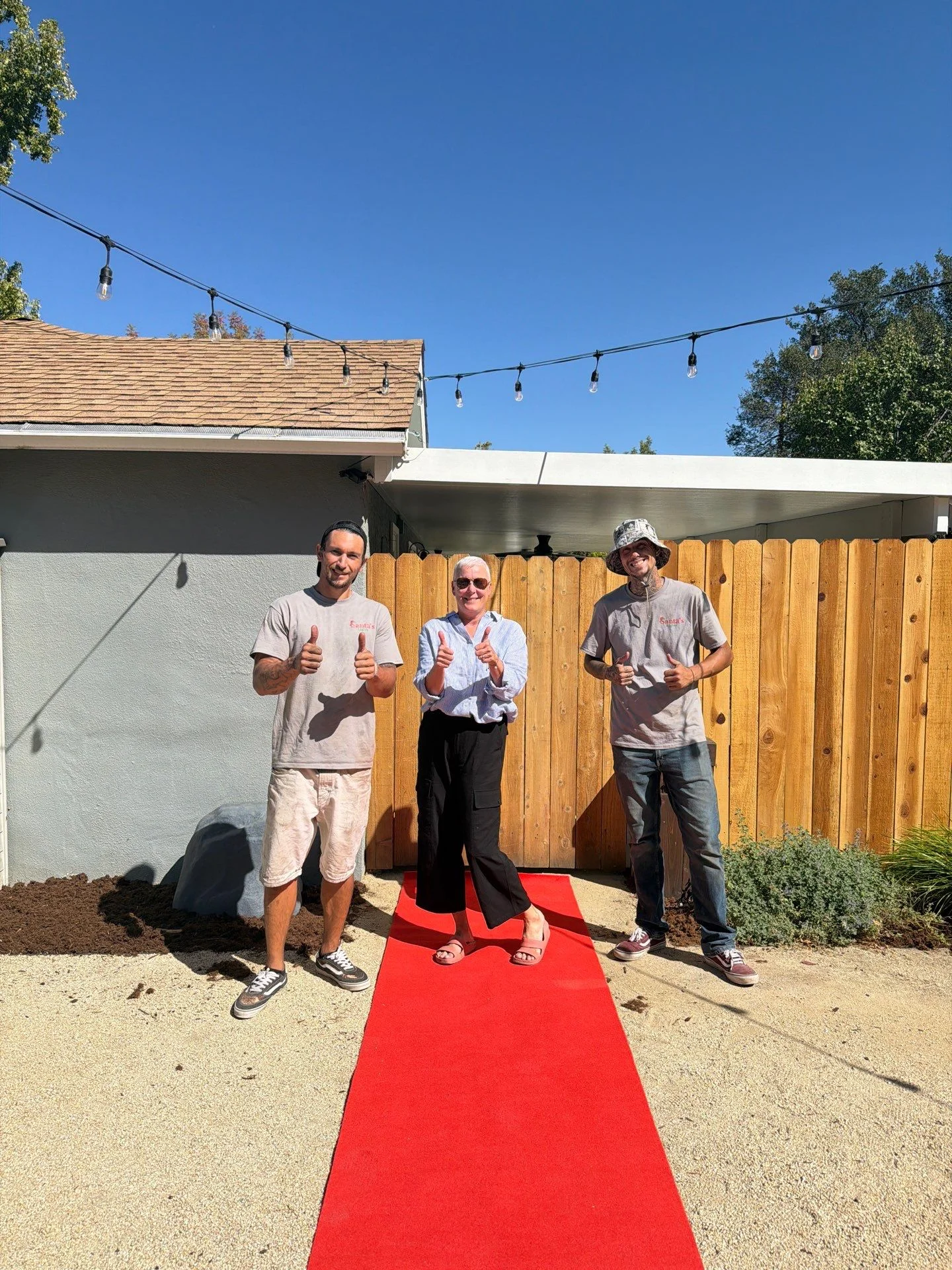Santa's Lights crew members and a homeowner giving thumbs up on a red carpet in a Fair Oaks backyard