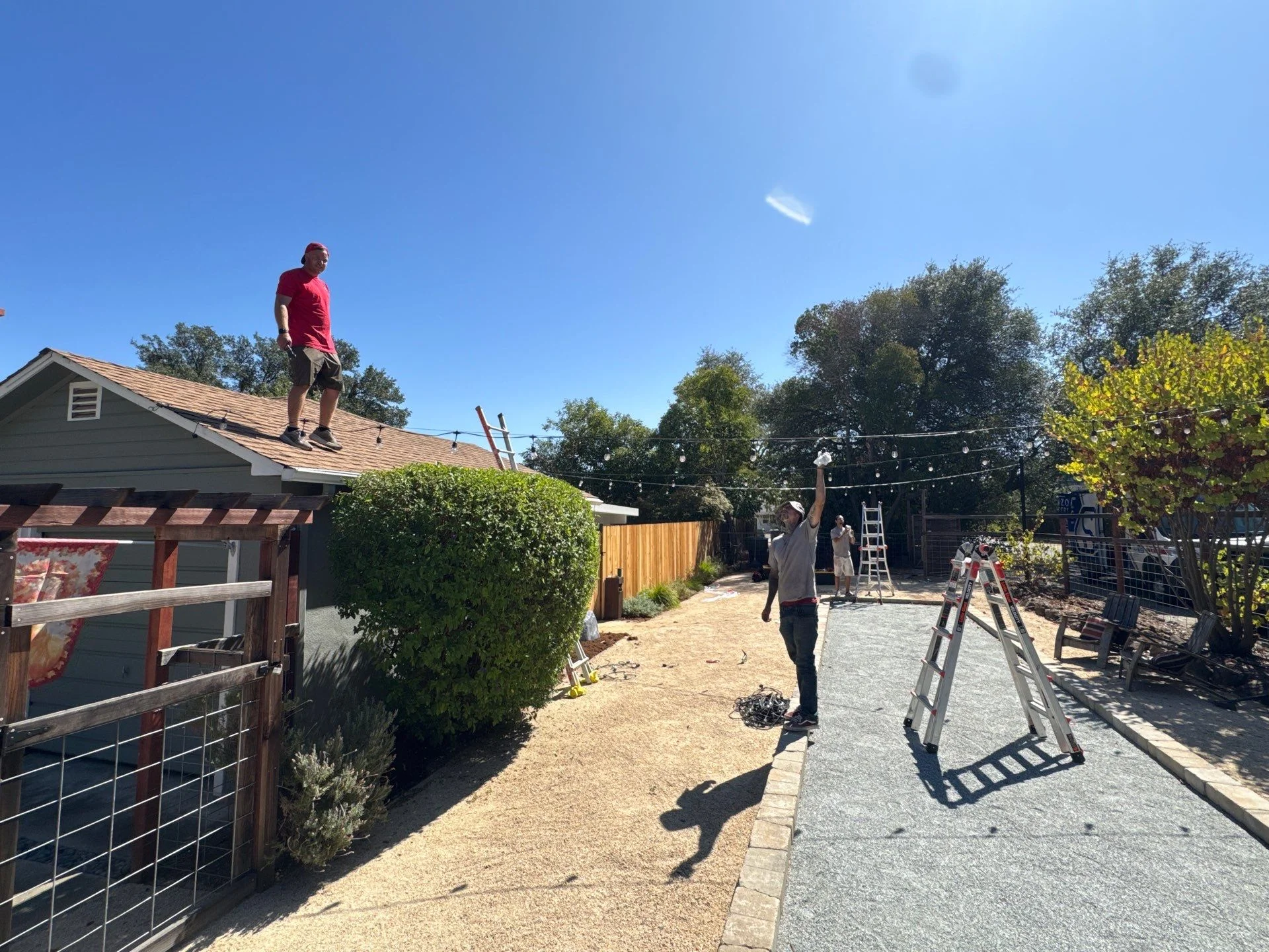 Crew installing string lights from a garage roof and ladders over a backyard bocce court in Fair Oaks